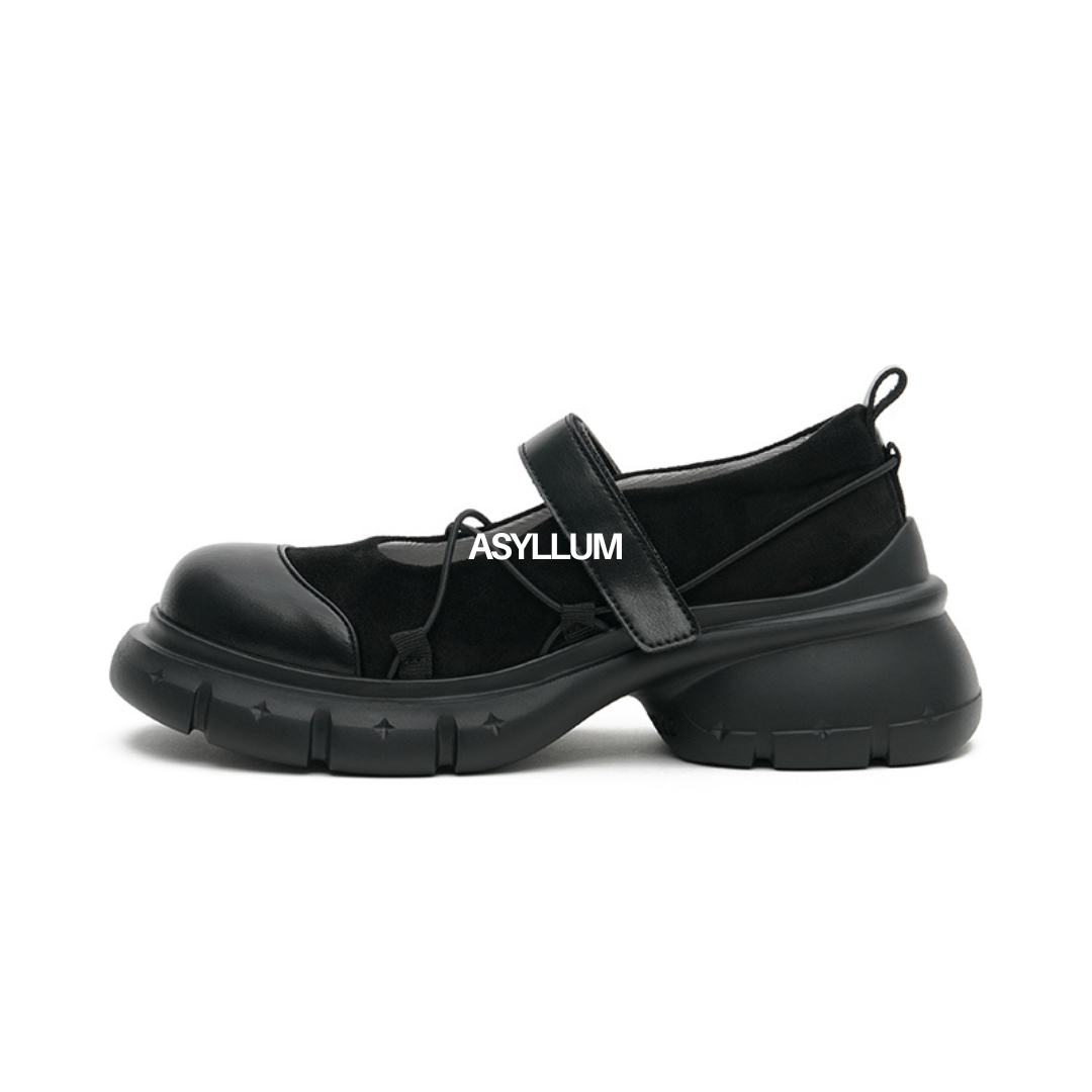 A black Mary Jane sneaker with a wide toe box and a strap featuring the brand name 'ASYLLUM'.