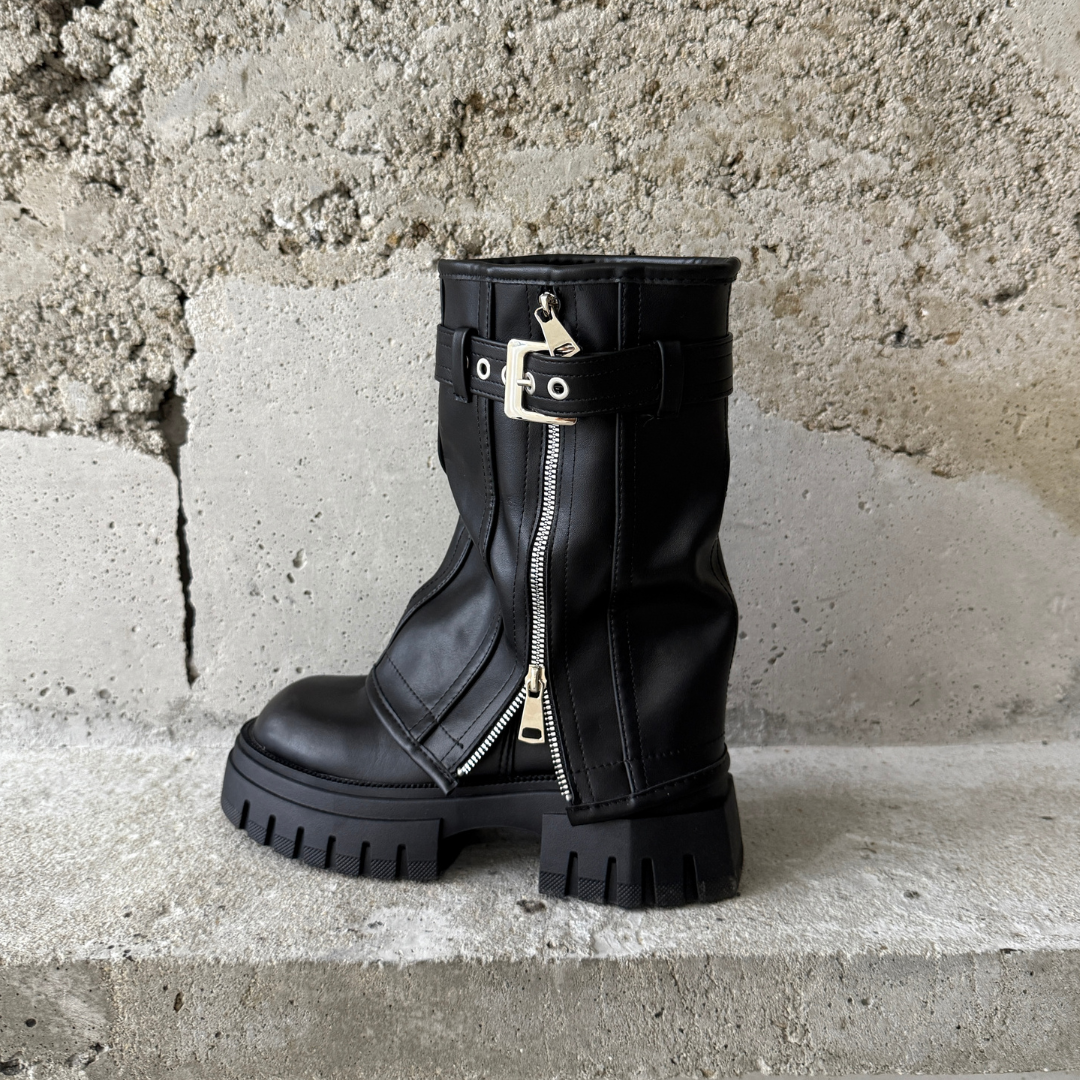 Black slouchy boot with a silver zipper on a concrete surface