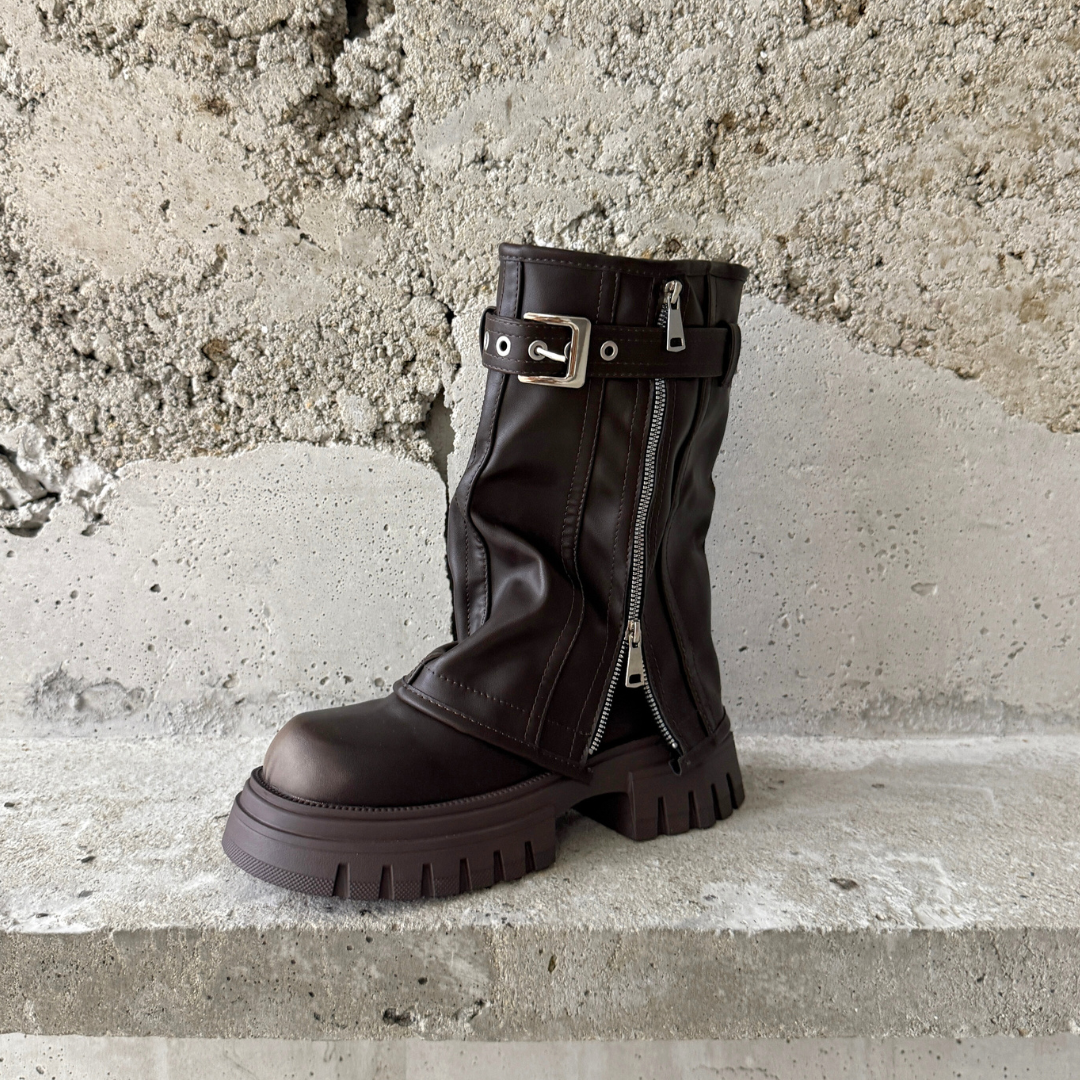 Dark brown slouchy boot with a silver zipper on a concrete surface